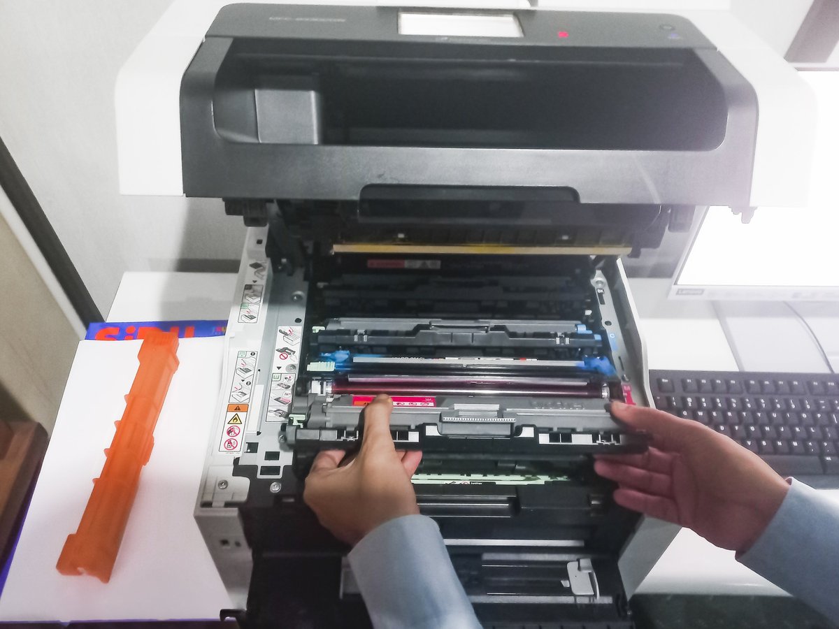 A man takes out a cartridge from a color laser printer for maintenance and refilling toner