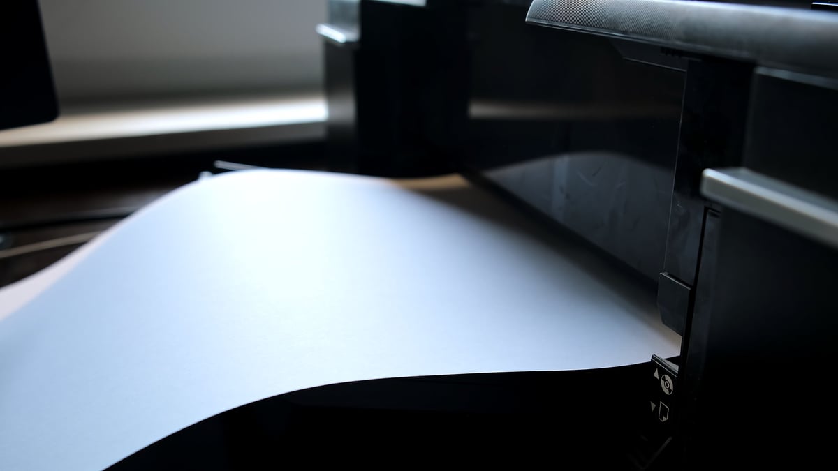 A printed paper sheet comes out of the color inkjet printer in close-up. Printing process.