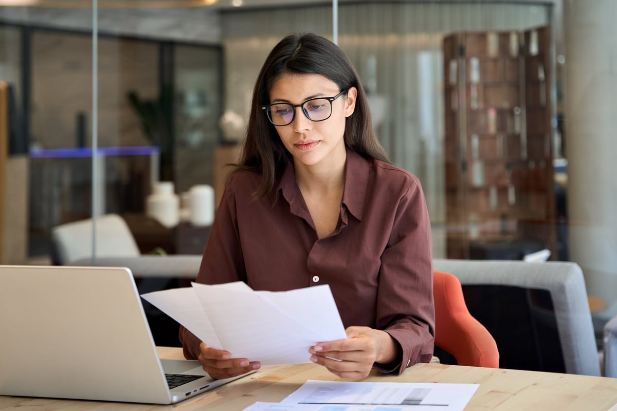 Focused latin hispanic business woman working on laptop computer reading financial document in office