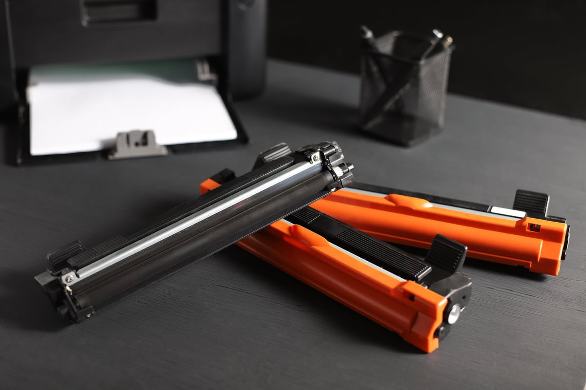 A set of toner cartridges for a laser printer with printer and white paper.