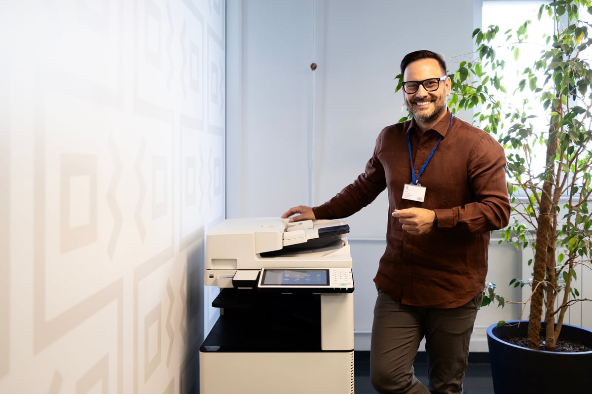 Happy male employee using modern multifunction printer in corporate office, smiling during work tasks.