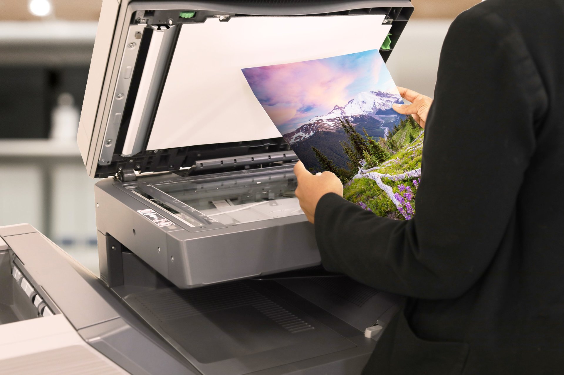 Person placing a photo of a mountain landscape into a flatbed scanner on a desk