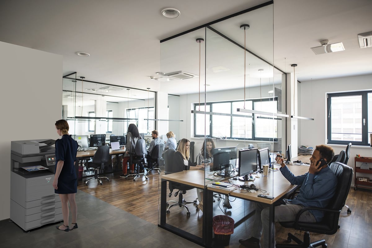 Modern open office with glass partitions, employees working at desks, and wooden flooring in a bright, contemporary workspace